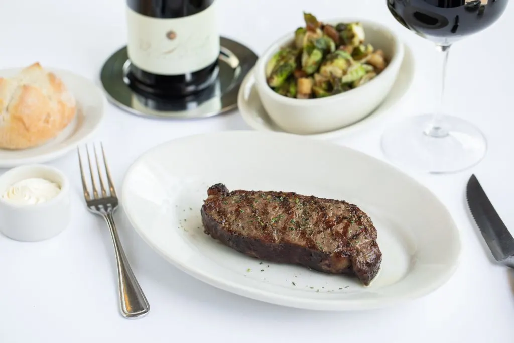 steak on a plate with a glass of wine and bread nearby