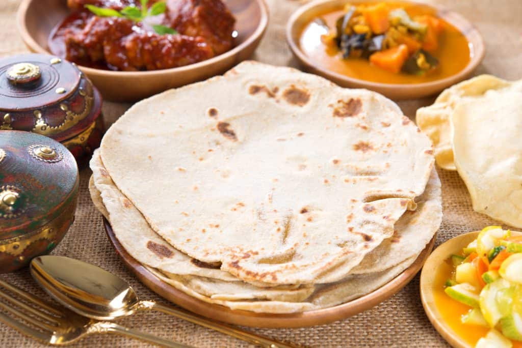 Traditional Indian flatbread with curry and vegetables on a rustic table.