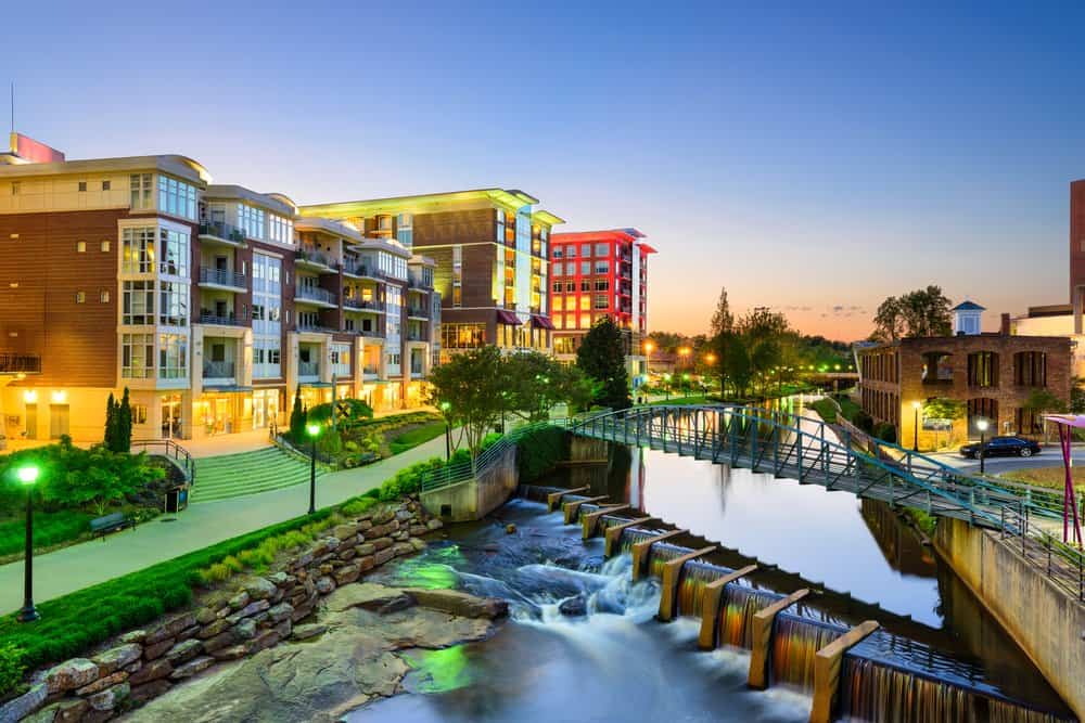 Modern apartment complex with a river and park at sunset.