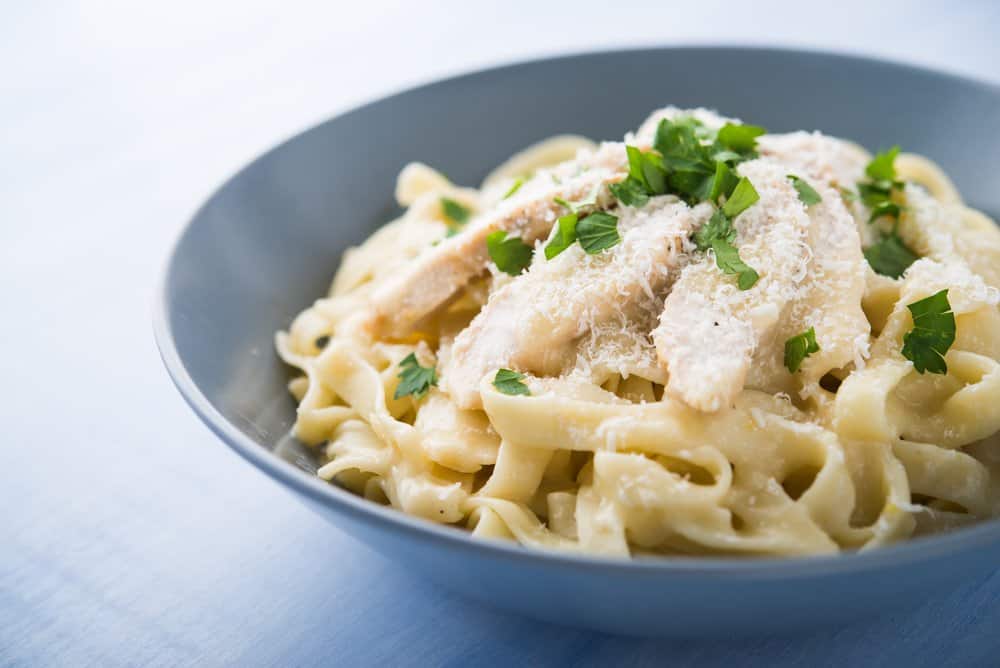 Creamy fettuccine pasta with grated cheese and chopped herbs in a blue bowl.