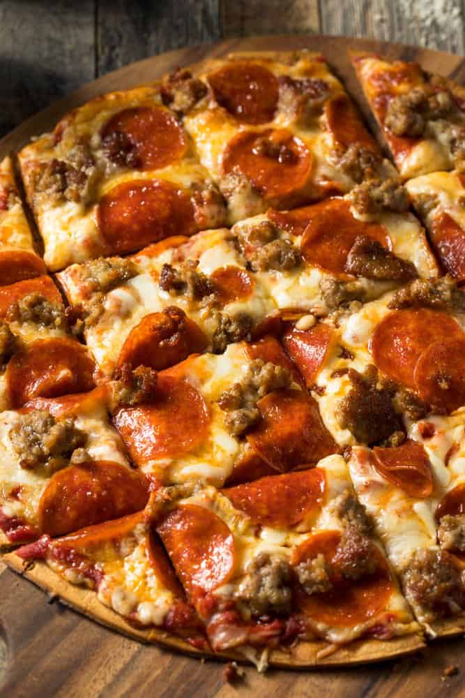 Delicious pepperoni and sausage pizza with melted cheese on a wooden board.