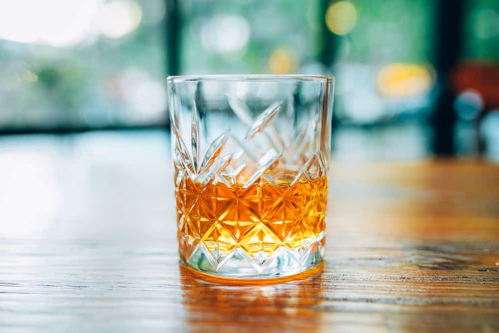 Glass of whiskey on a wooden table with blurred background.