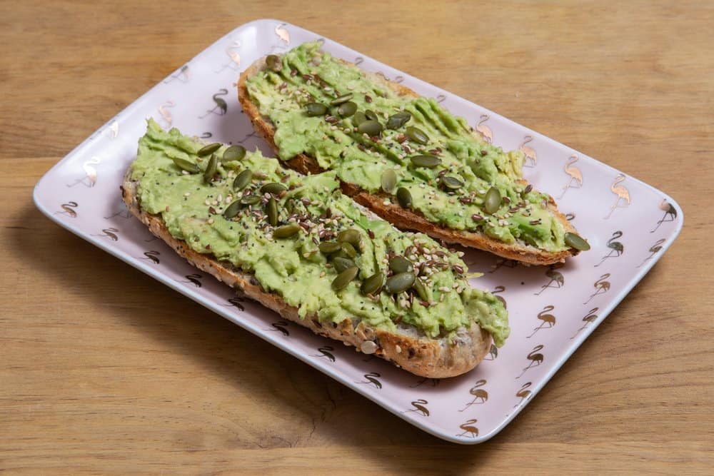 Avocado toast with pumpkin seeds on a white flamingo-patterned plate.