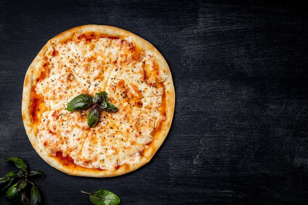 Cheese pizza with basil leaves on a dark background.