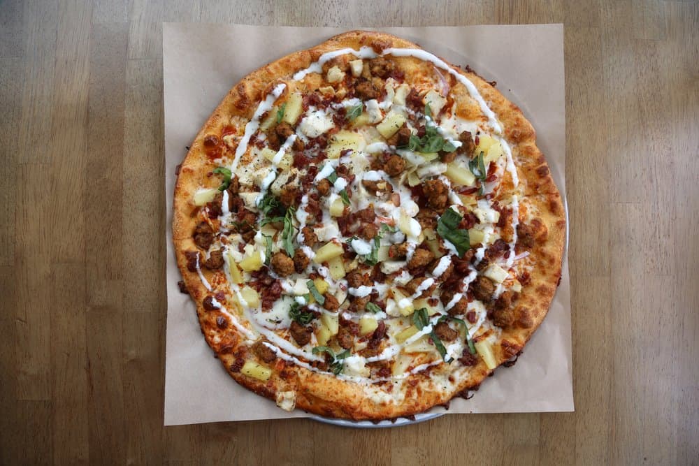 Delicious pizza topped with cheese, ground meat, and fresh herbs on a wooden table.