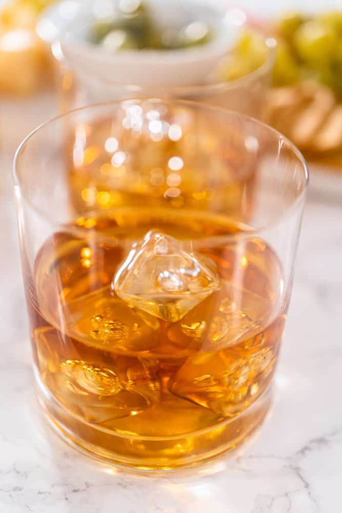 Glass of whiskey with ice cubes on a marble surface.