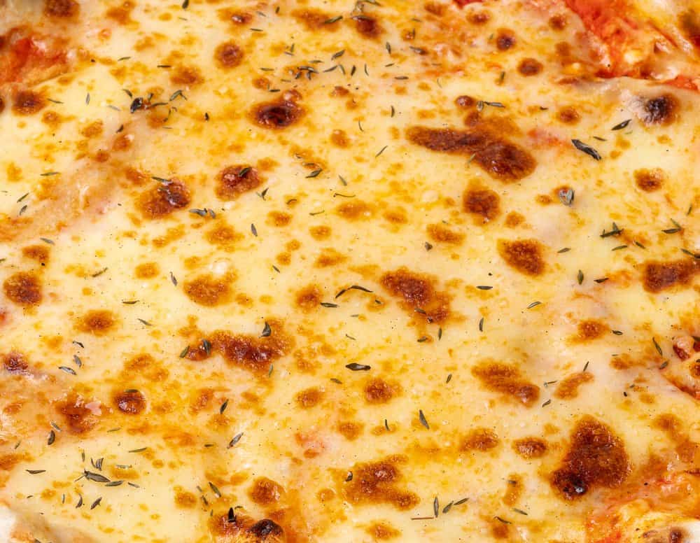 Close-up of cheesy pizza with herbs and golden-brown crust.