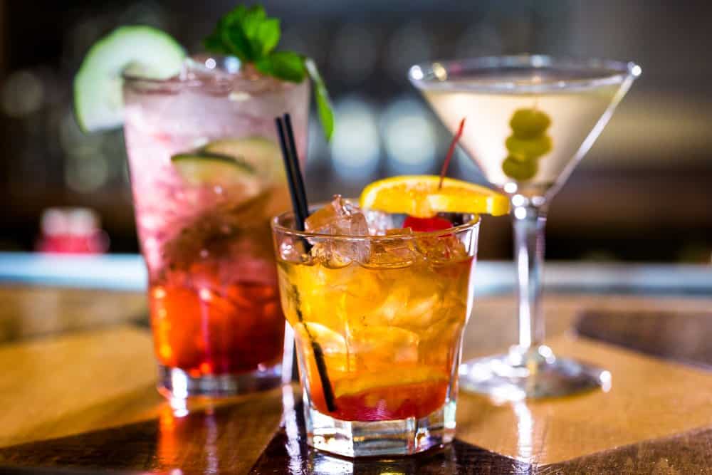 Colorful cocktails on a bar counter with ice and garnishes.