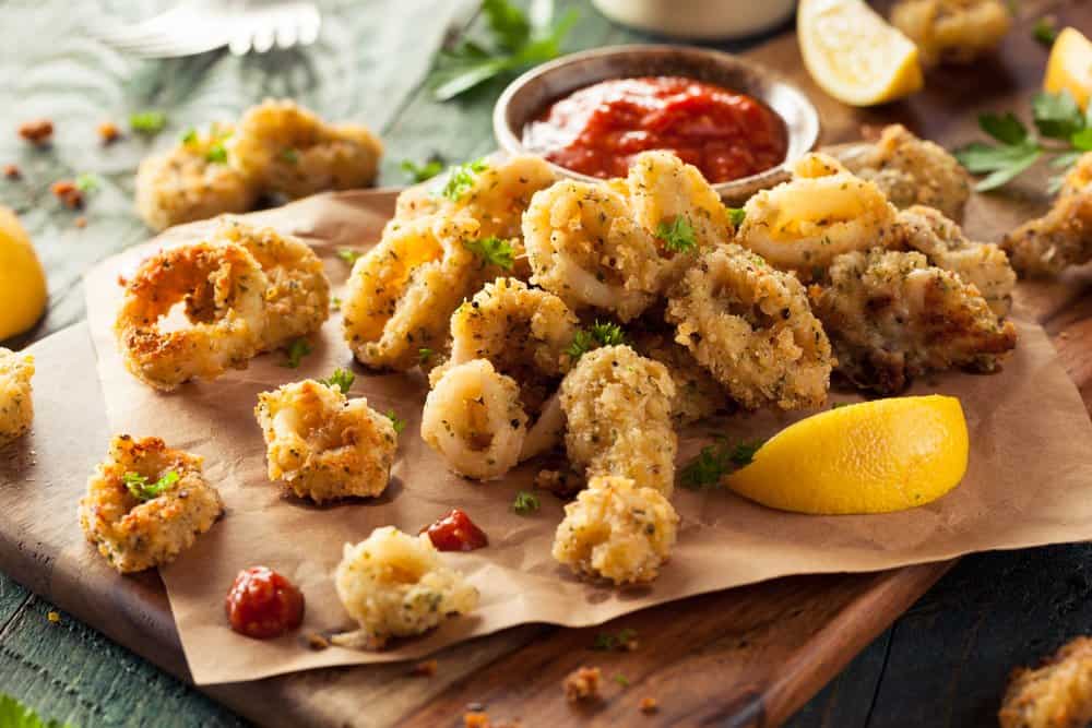 Crispy fried calamari with lemon wedges and dipping sauce on a wooden board.