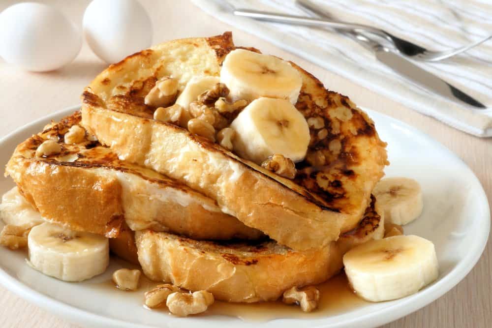 Delicious French toast topped with bananas and nuts on a white plate.