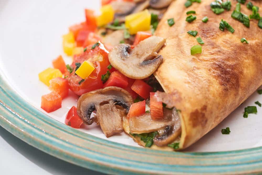 Delicious mushroom and vegetable stuffed crepe on a white plate.