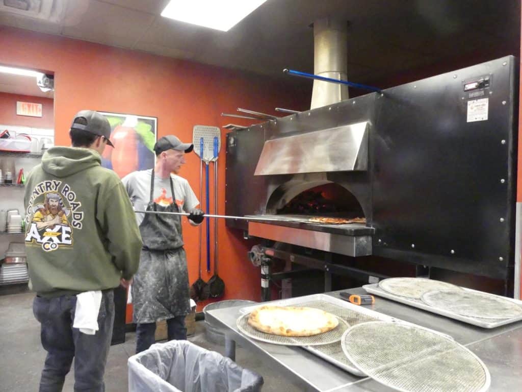 Chef preparing pizza in a professional kitchen with customers watching.