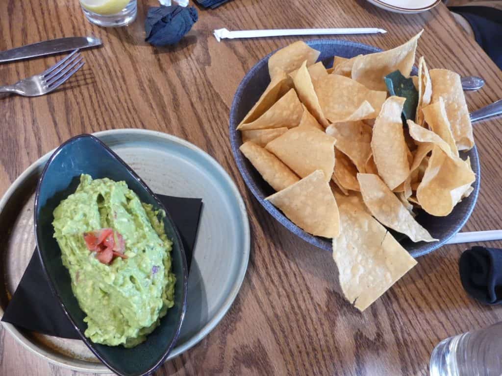 Fresh guacamole with tortilla chips on a wooden table at a restaurant.