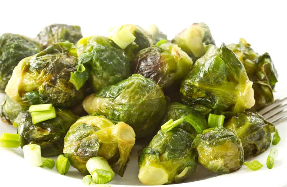 Close-up of cooked Brussels sprouts with chopped green onions on white background.