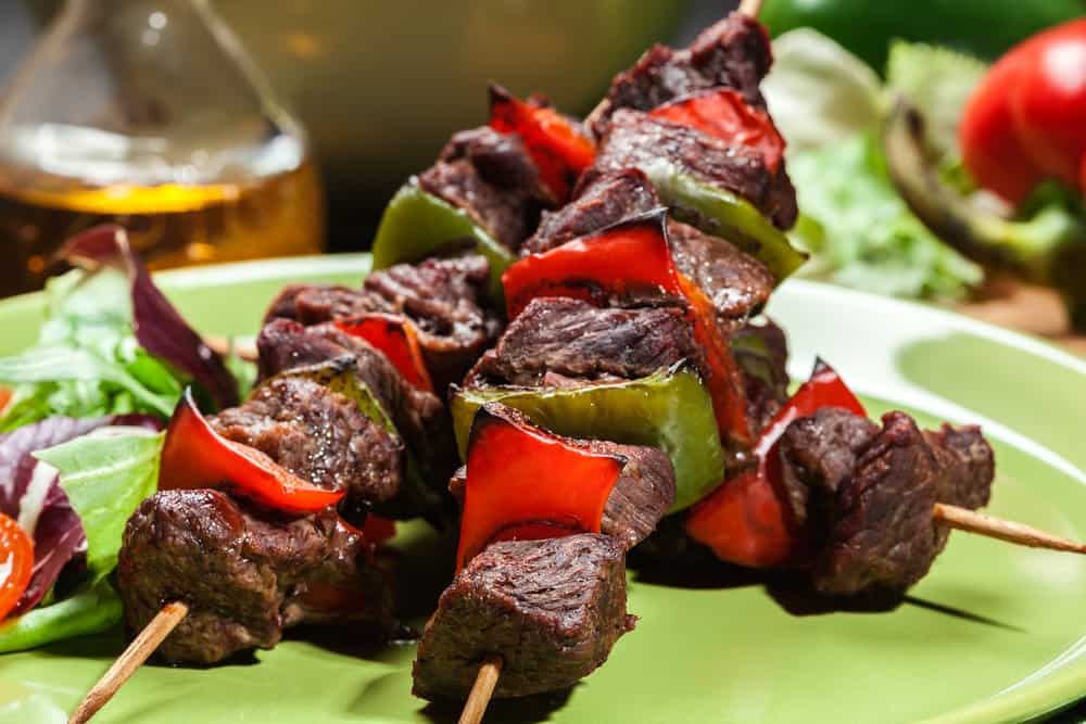 Beef and vegetable skewers on a green plate with fresh salad.