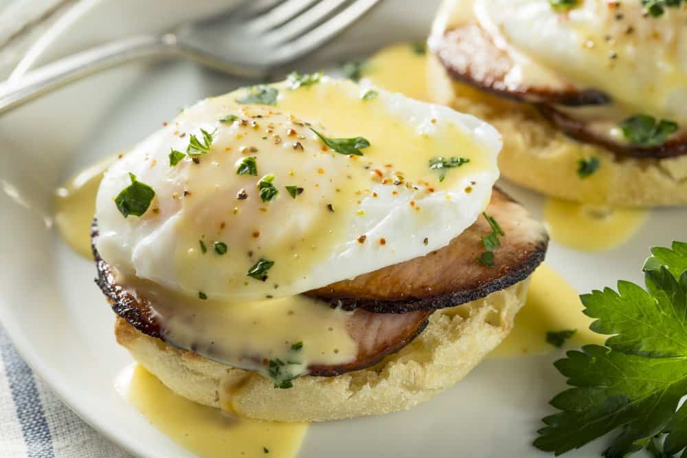 Delicious eggs Benedict with ham and hollandaise sauce on a white plate.