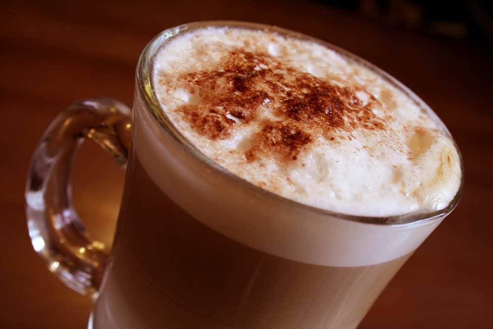 Hot chocolate with whipped cream and cinnamon on top in a glass mug.