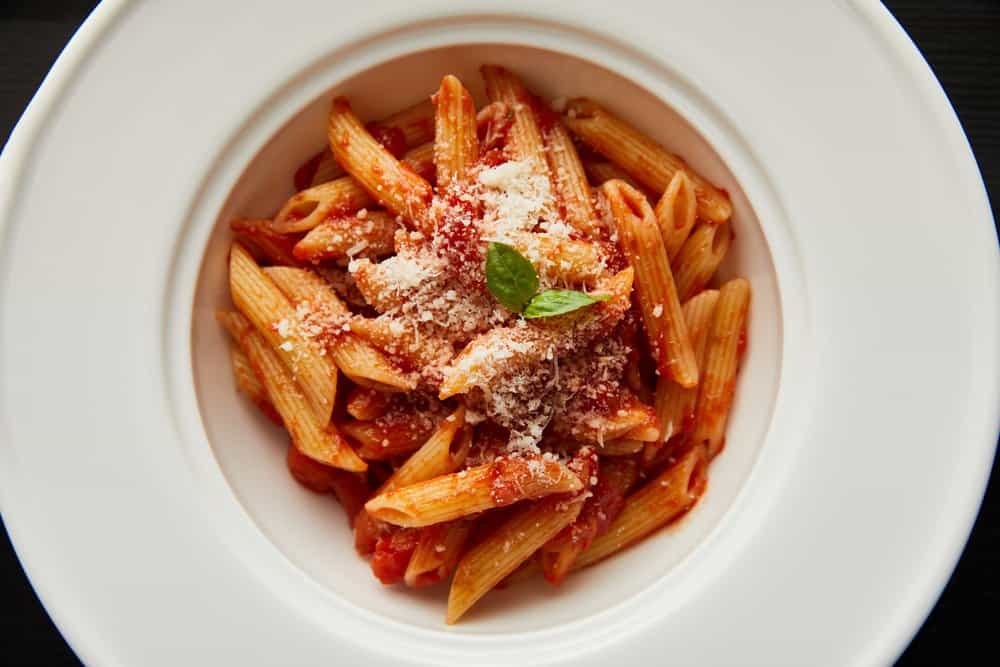 Delicious penne pasta with tomato sauce, grated cheese, and basil on a white plate.