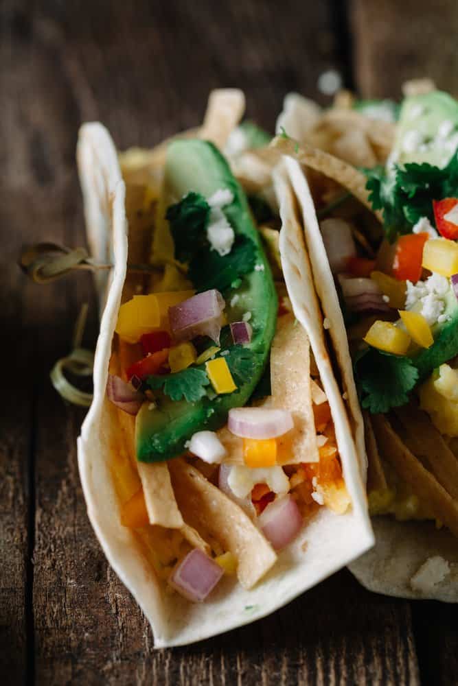 Fresh tacos with vegetables and herbs on a rustic wooden surface.