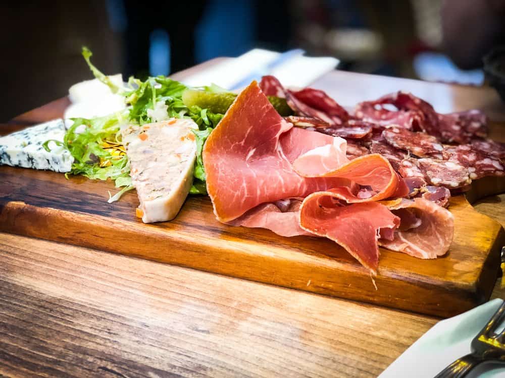 Assorted cured meats and cheeses on a wooden platter with greens.
