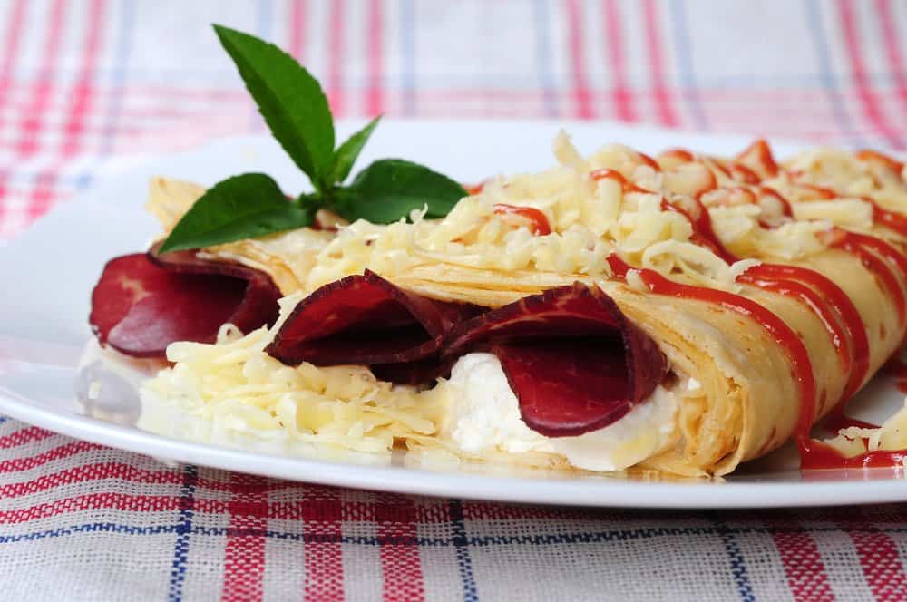 Strawberry and cream crepe with mint garnish on a plate.