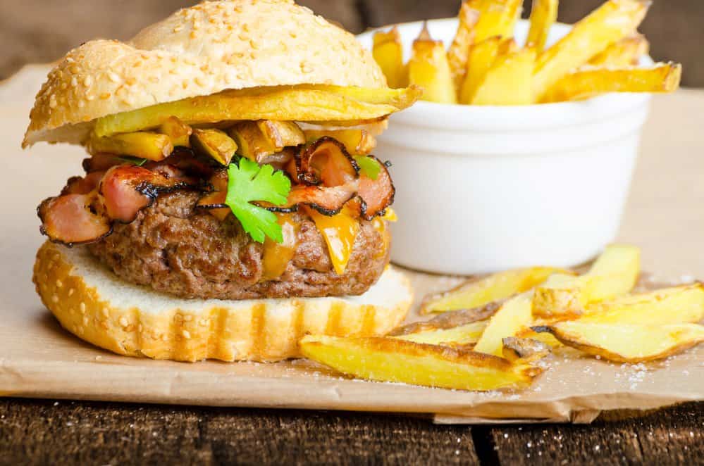 Juicy burger with fries on a rustic wooden board.