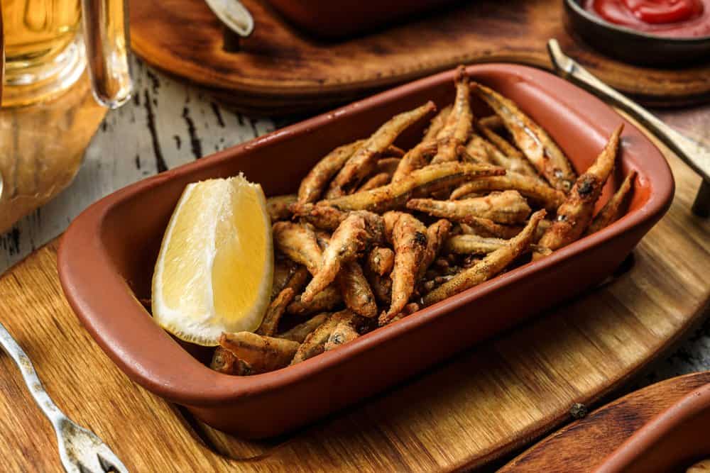 Crispy fried small fish with lemon wedge on a rustic wooden table.