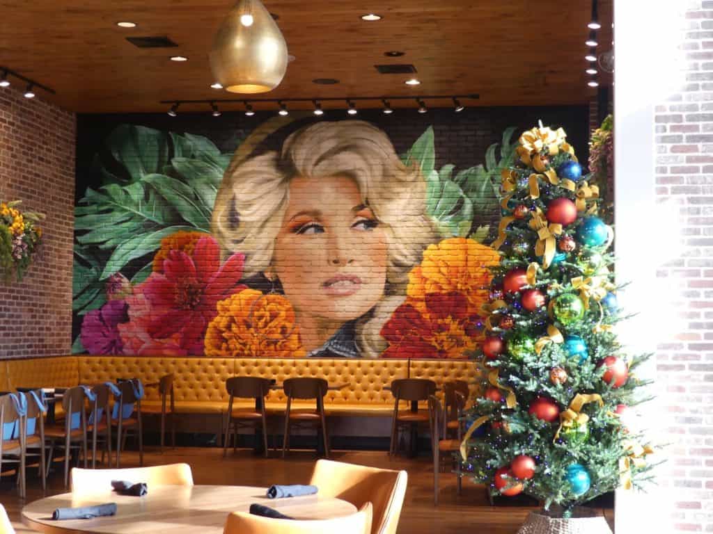 Decorated Christmas tree in a cozy restaurant with mural of a woman and flowers.