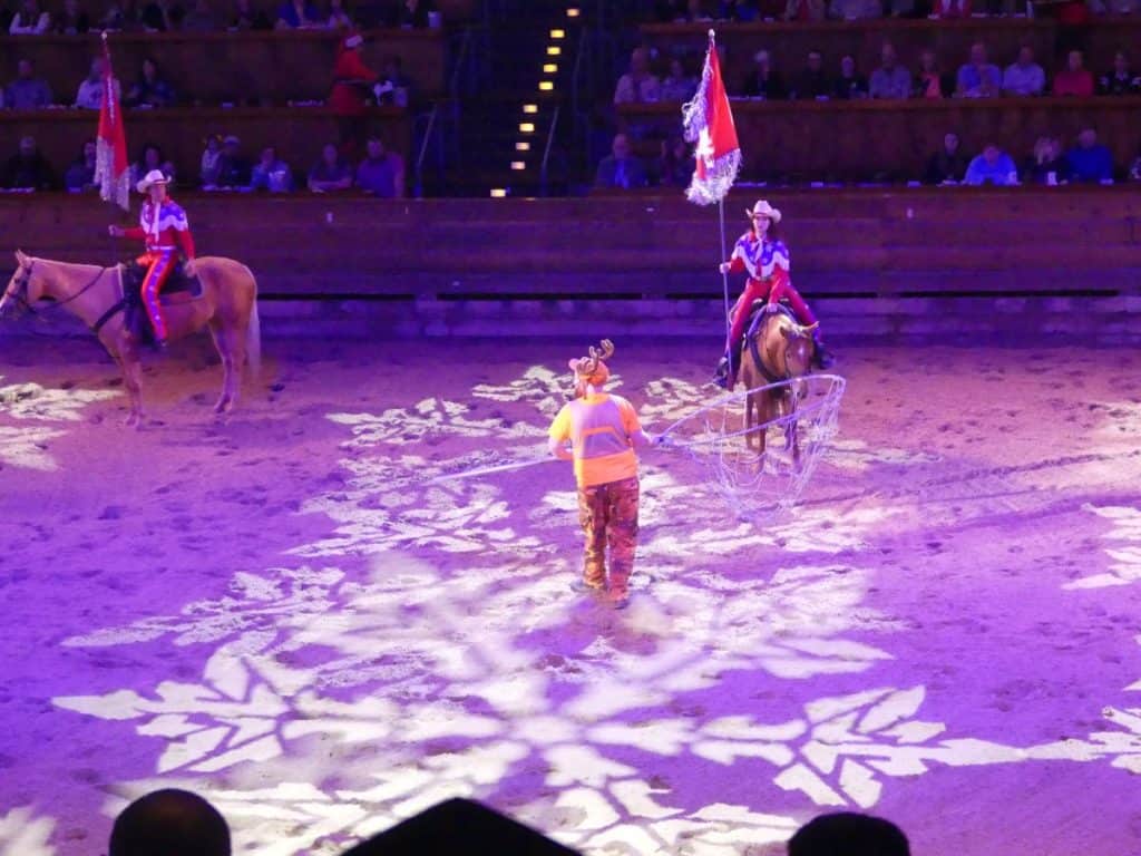 Circus performers on horseback with snowflake patterns projected on the ground.