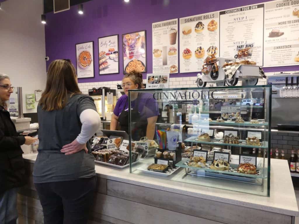 Foodie Flashpacker bakery display with assorted baked goods and customers.