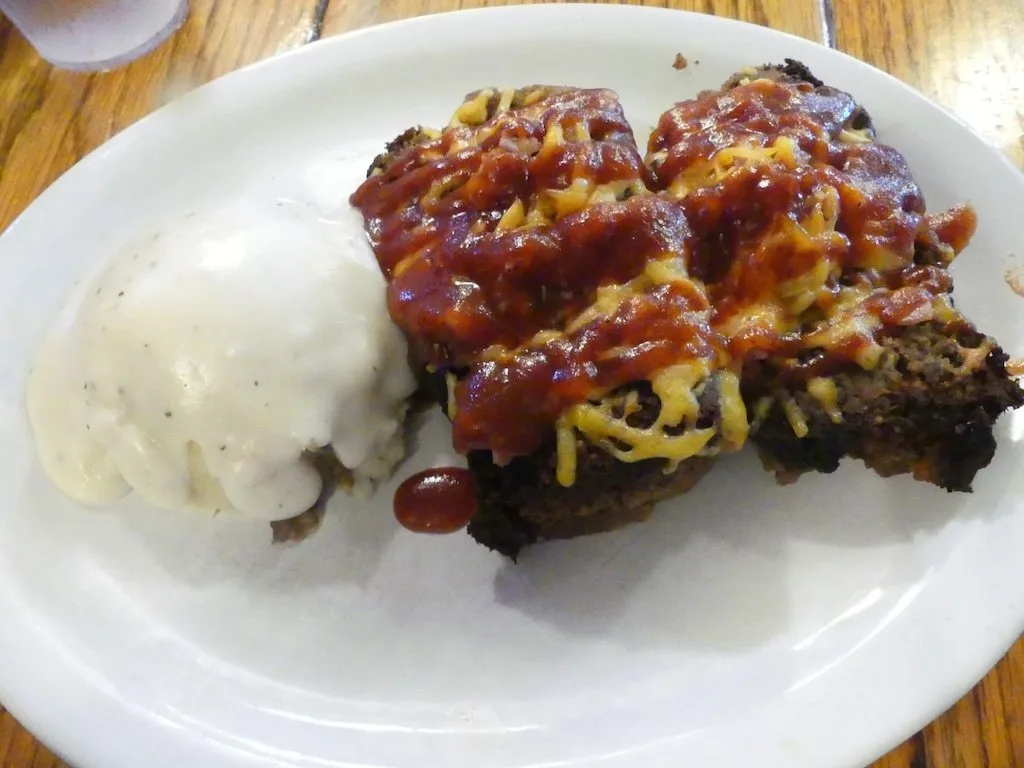meatloaf on a plate covered in cheese and ketchup with a side of mashed potatoes and gravy