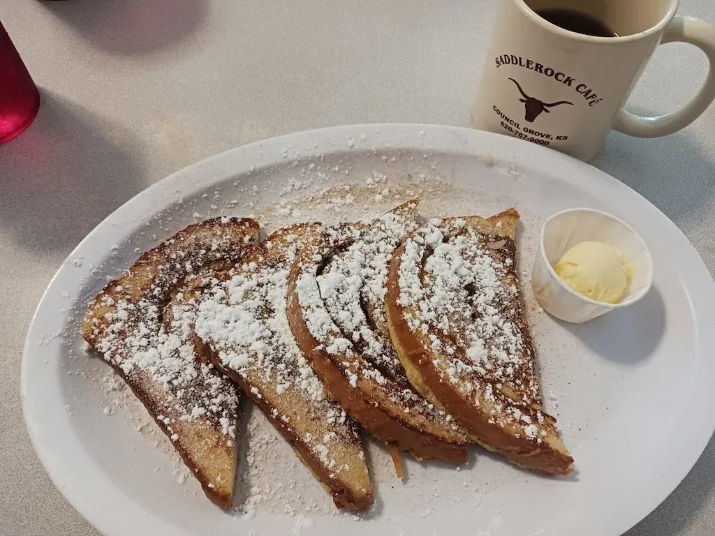 French toast on a plate with butter and a cup of coffee in the background